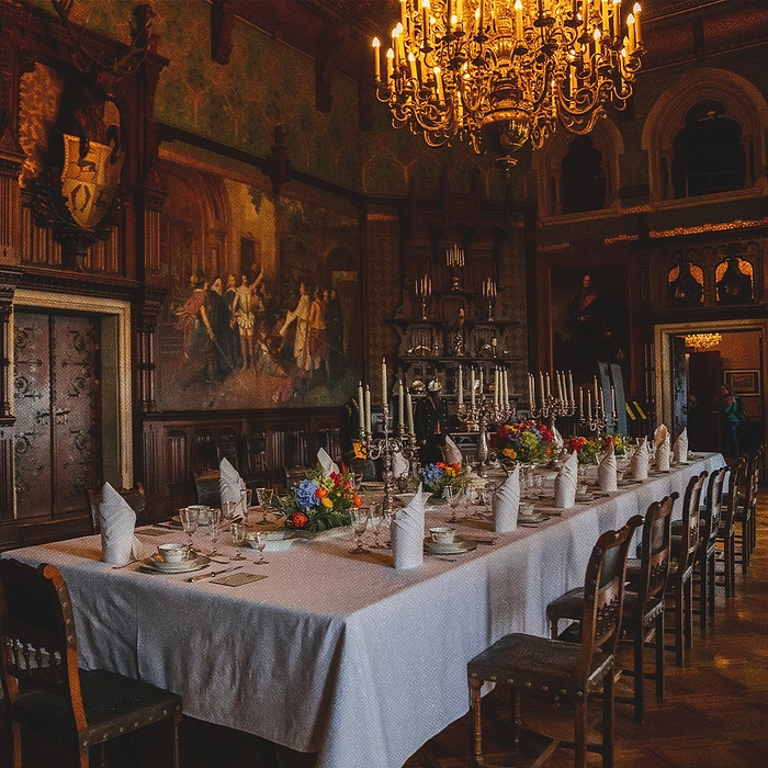 Intérieur d’une salle à manger de château salle à manger avec table longue et porcelaine dorée, assiettes et verres, candélabre dorée.