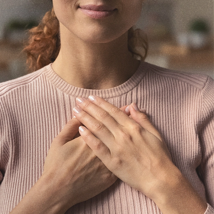 Close-up of woman holding her hands over her heart.