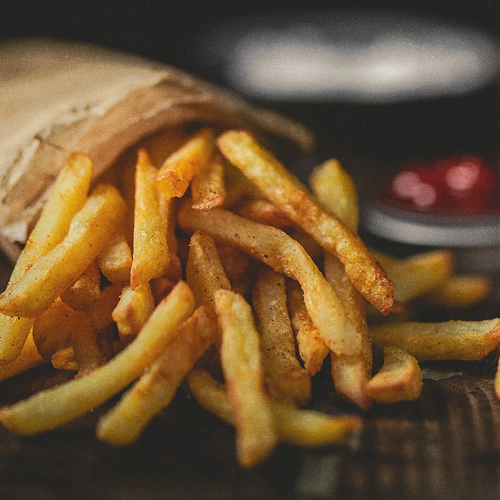 Frites dans un emballage en papier avec un pot de ketchup en arrière-plan.