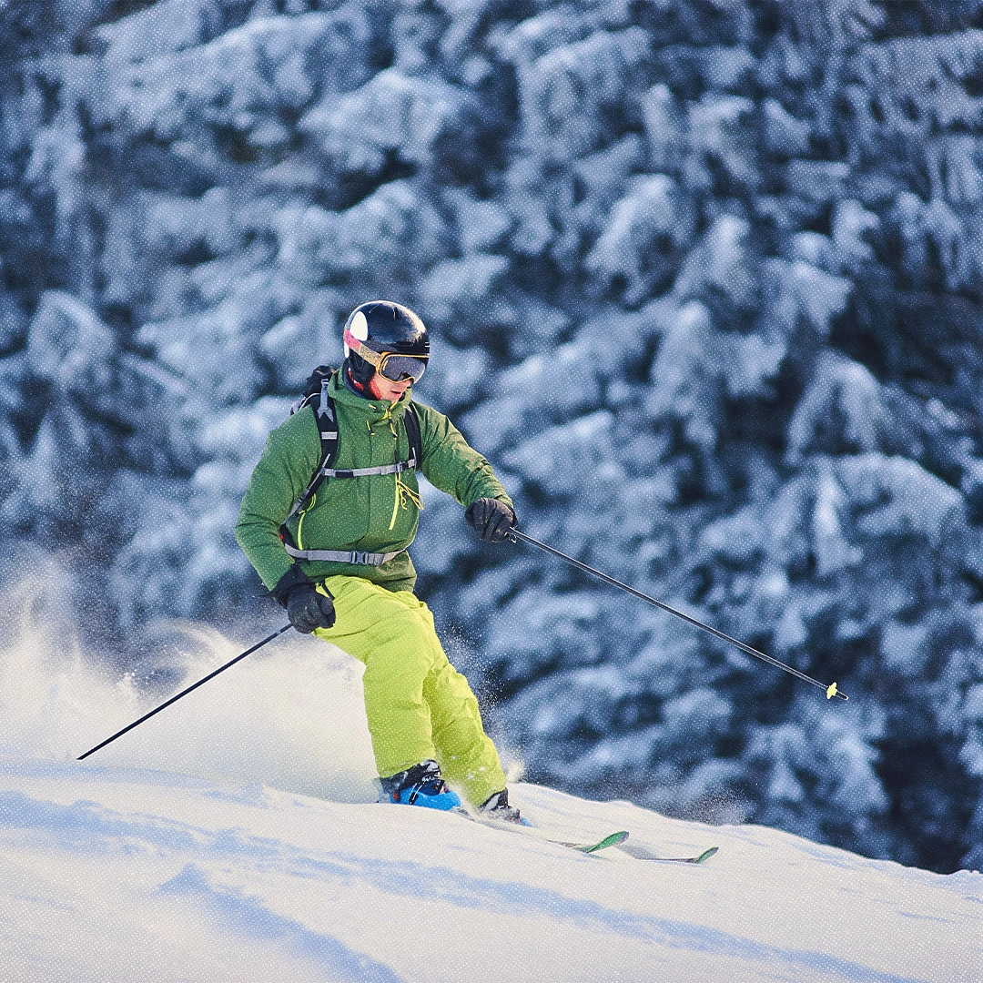 An alpine skier descends a snowy wooded mountainside.