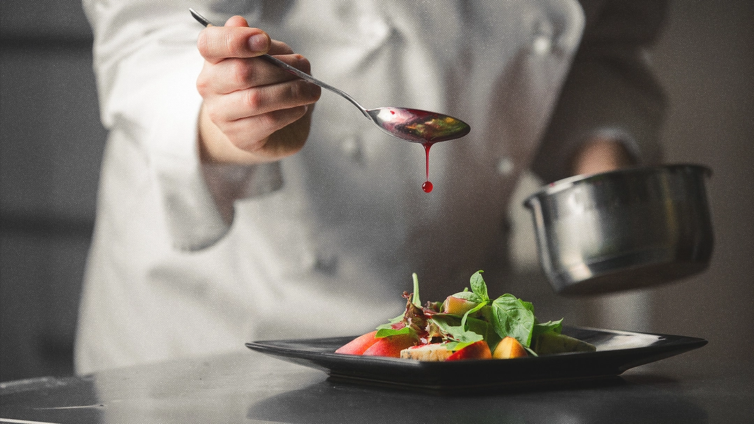 Chef cuisinier avec une cuillière dans la main et faisant couler son contenu sur un plat.