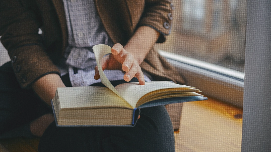 Un lecteur tient un livre sur ses genoux et tourne une page.