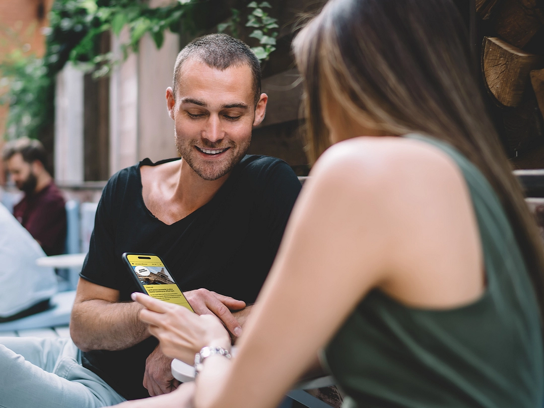 Femme de dos jouant à QuipoQuiz sur un téléphone portable avec son ami assis en face d'elle.